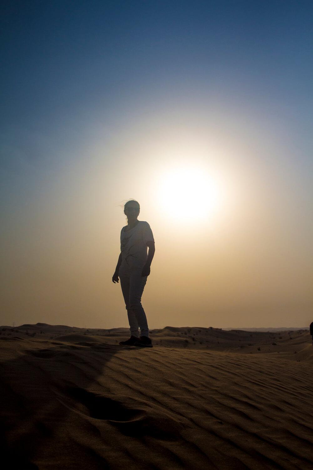 A person stood in the desert looking out past the camera with a sunset behind them